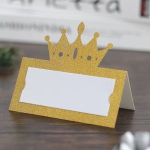 Detail of glitter gold crown place card with white nametag on dark wood background