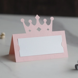 Gros plan d'un marque-place couronne rose ajourée avec papier perlé et insert vierge