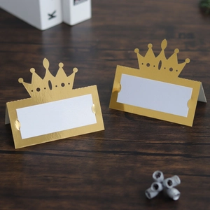 Detail of laser-cut gold crown place cards with white name inserts on a wooden surface