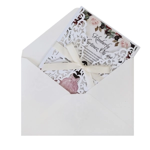Macro shot of laser-cut floral wedding invitation with white ribbon bow and envelope