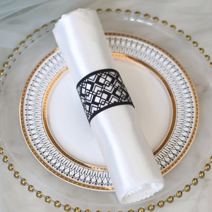 Macro detail of laser-cut black geometric napkin ring on white satin fabric napkin