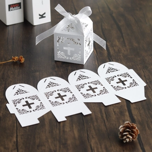 Close-up of white laser-cut cross wedding favors box with elegant floral pattern and ribbon