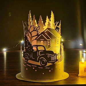 Close-up of laser-cut white paper lamp shade with Christmas tree truck and house