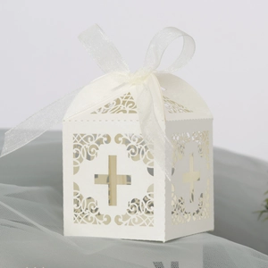 Detail of laser-cut cross pattern on white wedding favor box with a white silk ribbon bow
