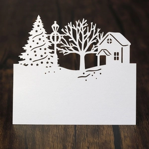 Detail of laser-cut Christmas tree and house patterns on a white pearlescent paper table card