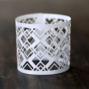 Macro detail of white laser-cut hollow napkin ring with geometric pattern on dark wood