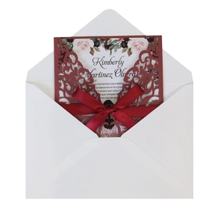 Detail of laser-cut floral wedding invitation with a red satin bow and inner card