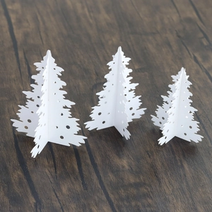 Set of 3 white 3D paper Christmas trees with laser cutouts on a dark wood background