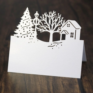 Laser cut white paper Christmas house place card with stars and tree on wood desk