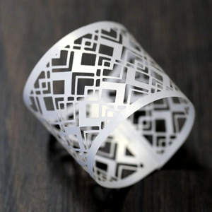 Close-up of laser-cut white paper napkin ring with hollow geometric pattern on wood
