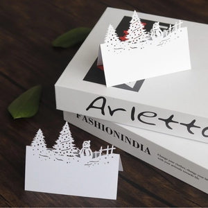Laser cut white 3D Christmas table cards featuring snowman and tree on wood background