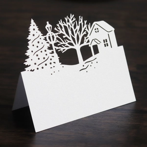 Detail of laser cut Christmas tree and house design on white pearlescent paper table card