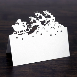 Detailed laser-cut white Santa and reindeer sleigh table card on wood background