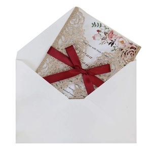 Macro detail of laser-cut gold glitter wedding invitation with red satin bow and floral insert