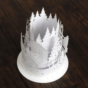 Detailed top view of white hollowed paper lampshade with winter forest and house motifs