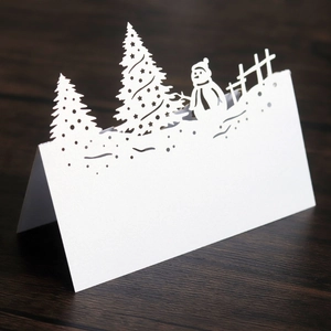 Detail of laser-cut white snowman and Christmas tree card on a dark wood surface