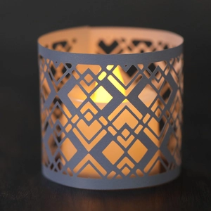 Macro detail of geometric hollow candle wrap with warm LED light and paper laser-cut design