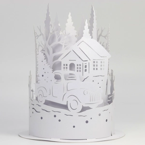 Detail of laser-cut white paper lampshade showing a 3D winter scene with truck and trees