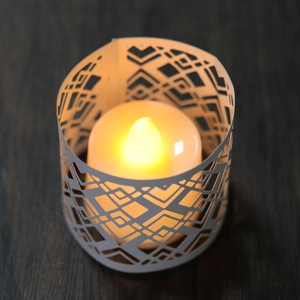 Macro view of LED candle with white geometric hollow paper lampshade on wood surface