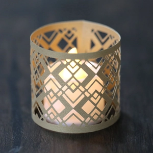 Geometric cutout paper lantern with warm LED candle light on wooden background