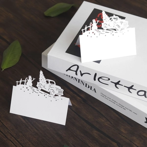 Laser cut white Christmas place cards with snowman and truck design on wood background