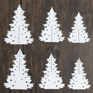 Macro view of white laser-cut paper Christmas tree ornaments set on wood background
