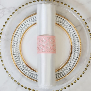 Close-up of pink laser-cut paper napkin ring with geometric patterns on a white napkin