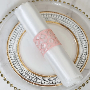 Pink laser-cut paper napkin ring with geometric patterns on a white satin cloth