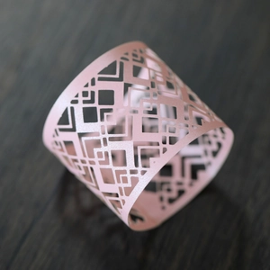 Macro shot of laser-cut light pink napkin ring with pearlescent finish on dark wood