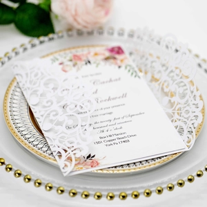 Close-up of laser-cut lace invitation cover and floral card on a gold-rimmed plate