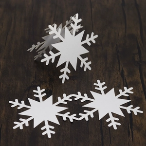 Three white snowflake place cards for festive table settings on dark wood background