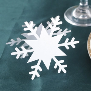 Detailed view of laser-cut white snowflake place cards on a dark green velvet surface