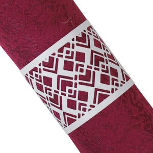 Detail of white laser-cut geometric napkin ring on deep red jacquard fabric