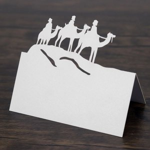 Detail of laser-cut white camel silhouette place card on a dark wooden background