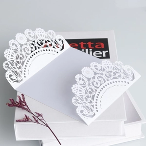 Macro detail of laser-cut wedding invitation with intricate lace patterns on white pearlescent paper