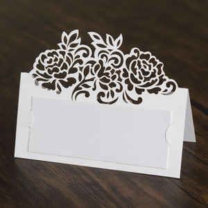 Macro detail of white laser-cut floral place card on elegant dark wood table texture
