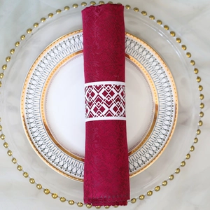 Detail of laser-cut white paper napkin ring on burgundy jacquard cloth and gold rimmed plate