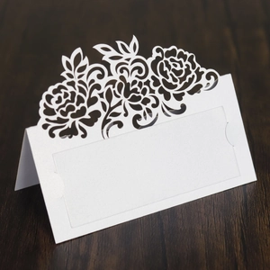 Detailed laser cut rose design on white pearlescent paper wedding place card on wood background