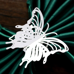 Close-up of white laser-cut butterfly napkin ring on green satin and wood background