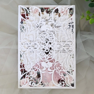 Macro shot of white laser-cut wedding invitation with vintage floral inner page and lace