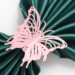 Detail of pink laser-cut butterfly napkin ring on green satin for wedding decor