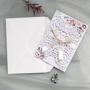 Detail of laser cut wedding invitation with floral insert and cream satin bow