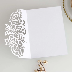 Macro detail of laser-cut white rose floral lace pattern on wedding invitation card