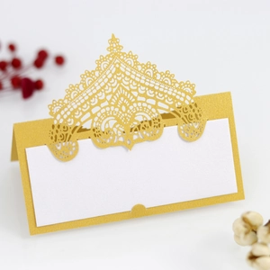 Macro detail of gold laser-cut lace place card with elegant hollow crown design on pearl paper