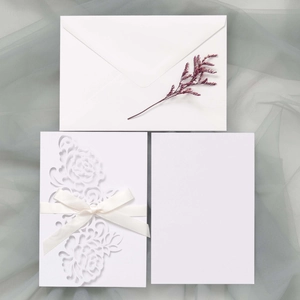 Detailed laser-cut white floral wedding invitation with white satin bow and envelope