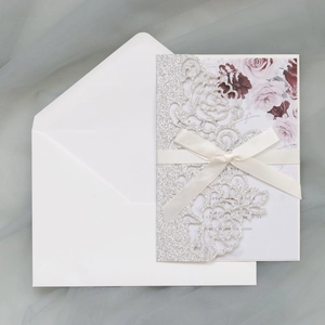 Detail of laser cut silver glitter invitation with ribbon and floral rose inner card