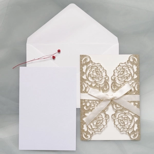 Close-up of laser-cut champagne gold glitter invitation with white bow and envelope