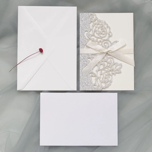 Detail of laser-cut floral wedding invitation with silver glitter and satin ribbon bow