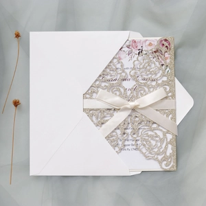 Macro detail of laser-cut gold glitter invitation with cream ribbon and floral inner card