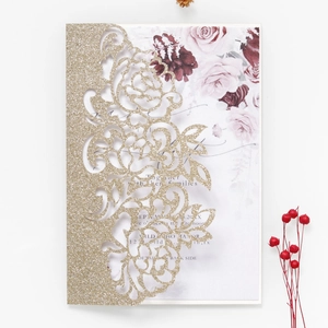Close-up of laser-cut gold glitter invitation with elegant rose pattern and floral inner card